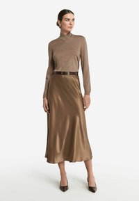 Haut en tricot brun avec un col haut, associé à une jupe midi en satin brun. Apparence texturée et lisse avec une taille ceinturée et des talons pointus.