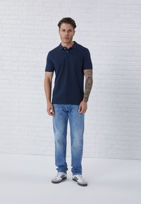 Navy blue polo shirt with short sleeves and a collar, paired with light blue jeans and white sneakers with black stripes.