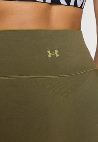 Zöld sportos leggings, rugalmas anyagból készült, elasztikus derékrésszel és a felső részén egy ellentétes színű kis logóval.