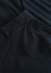 Sötét tengerészkék nadrág, összehajtva bemutatva, sima textúrával, finom csillogással, egyenes szabással, szabványos derékrésszel és zsebekkel.