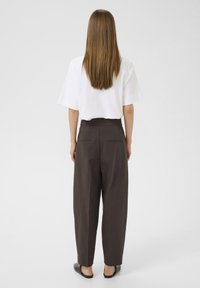 Camicetta bianca a maniche corte con una vestibilità rilassata, abbinata a pantaloni marroni scuri a vita alta con due tasche posteriori. Texture del tessuto liscia.