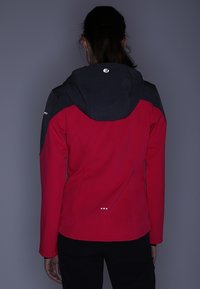 Giacca impermeabile rossa e nera con cappuccio, dal design aderente, con pannelli spalla a contrasto e dettagli riflettenti sulla schiena.