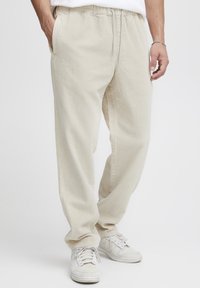 Pantalon en velours côtelé beige à coupe décontractée, doté d'une taille élastique, de poches latérales et d'une texture côtelée verticale discrète.