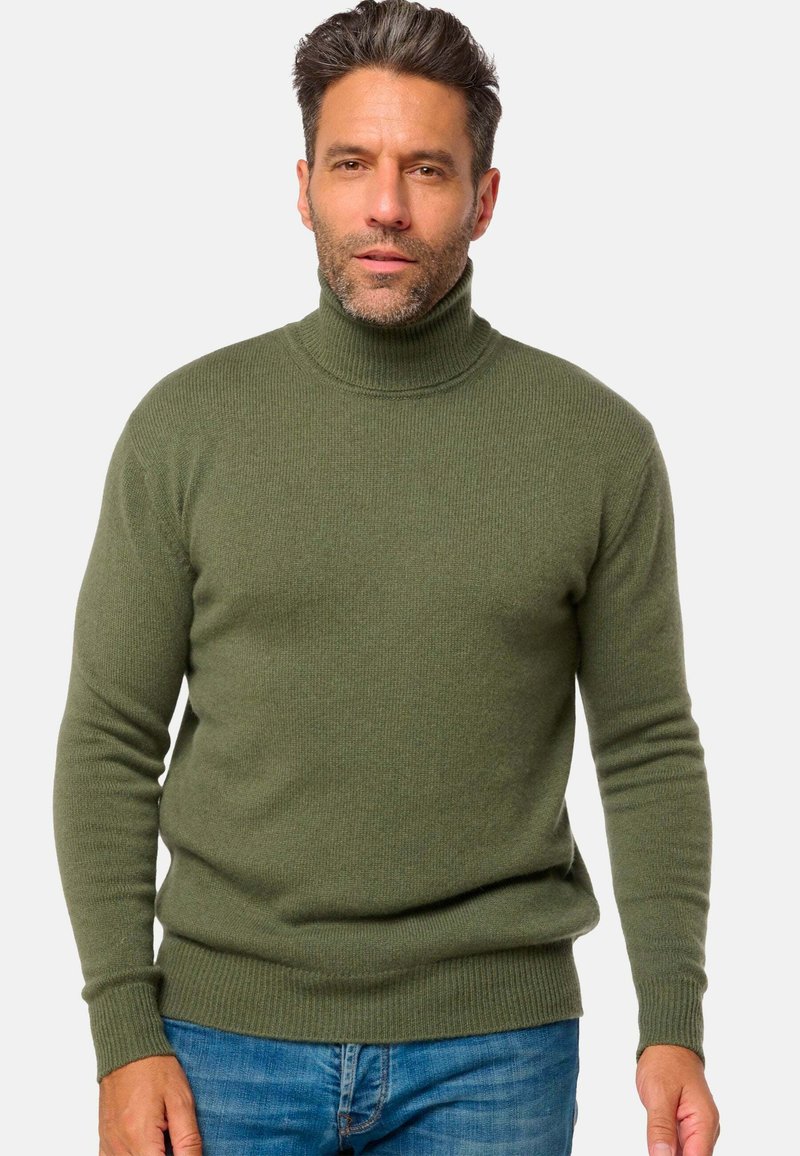 Pull à col roulé vert olive en texture côtelée avec manches longues, un design ajusté et un col haut, associé à un jean bleu.