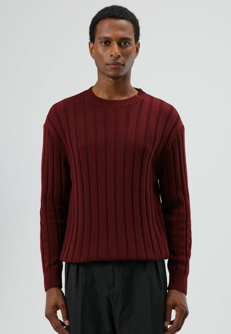 Bordeauxroter, gerippter Pullover mit langen Ärmeln, rundem Ausschnitt und strukturierter Stoffqualität. Lässige Passform mit horizontalem Streifenmuster am Körper.