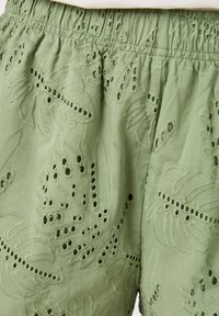 Shorts en coton verts avec des motifs floraux brodés et des découpes. Ceinture élastique avec texture froncée pour le confort.