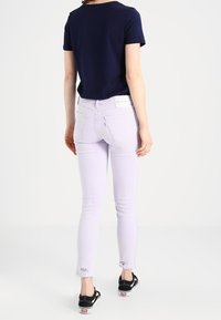 Jeans skinnies lila con dobladillo sin rematar, combinados con una camiseta de manga corta azul marino. Zapatillas negras visibles en los tobillos. Diseño sencillo y ajustado.