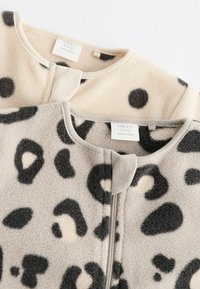 Zwei Baby-Fleecejacken, eine mit schwarzen Punkten auf Beige, die andere mit einem Leopardenmuster. Beide haben runde Ausschnitte und Reißverschluss.