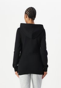 Černá mikina s žebrovaným lemem a manžetami. Obsahuje velkou kapuci a dlouhé rukávy. Materiál vypadá měkký a elastický.