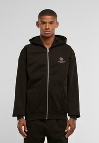 Felpa nera con zip realizzata in un morbido tessuto, dotata di una tasca a marsupio e di un piccolo logo sul lato sinistro del petto. Completata da pantaloni scuri abbinati.
