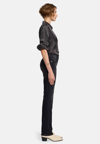 Svarta denimjeans i kombination med en mörk satinblus. Smal passform, uppvikta ärmar och ljusa ankelskor med spetsig tå.