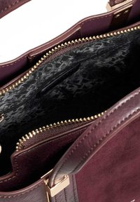 Bordeaux handtas met een glad leren buitenkant, gouden rits en een met een patroon bedekte zwarte voering; inclusief een ritszak en stevige handgrepen.