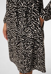 Robe à imprimé zèbre noir et blanc avec manches longues, poches et coupe décontractée, fabriquée à partir d'un tissu léger à la texture douce.