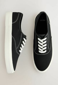 Sneakers in tela nera con lacci bianchi, cuciture bianche a contrasto e suola in gomma bianca testurizzata. Design semplice con punta arrotondata.