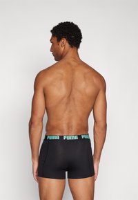 Black boxer briefs with a turquoise Puma logo on the elastic waistband, fitted design, and smooth fabric, viewed from the back.