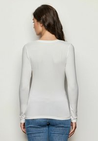 Weißes Langarmshirt aus elastischem Stoff mit rundem Ausschnitt, figurbetontem Schnitt und glatter Textur, kombiniert mit blauen Jeans.