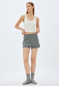 Witte geribbelde tanktop met knopen aan de voorkant, gecombineerd met grijze textuuroveralls met een kantaccent aan de onderrand. Grijze gebreide sokken.
