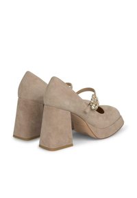 Pantofi cu toc din suede bej, cu vârf rotund și toc gros. Prezentă o cataramă decorativă cu accente clare pe cureaua laterală.