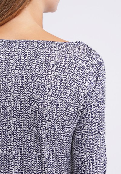 Haut bleu marine et blanc à motif avec un décolleté arrondi et des manches longues, présentant un tissu doux et texturé dans un design abstrait.