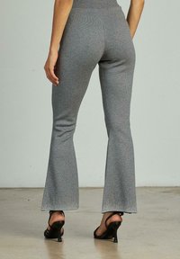 Grijze flare-broek met een glanzende textuur, voorzien van een hoge tailleband en subtiele versieringen, gedragen met zwarte, strapschoenen.