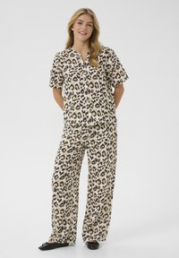 Ensemble de pyjama à imprimé léopard en beige et noir, comprenant un haut à manches courtes avec une patte de boutonnage et un pantalon ample à jambes larges.