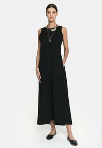 Czarny bezrękawnik z szerokimi nogawkami, wykonany z gładkiego materiału. Posiada boczne kieszenie i okrągły dekolt. Noszony z czarnymi płaskimi butami i łańcuszkiem na szyi.