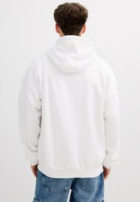 Sudadera blanca con capucha, de corte relajado y hombros caídos. Textura suave, puños y dobladillo con canalé, diseño sencillo.