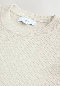 Bež pulover z vzorcem teksturiranih diamantov, rebrastim ovratnikom in etiketo z napisom "NEXT Slim Fit." Iz bombažnega materiala z mehkim zaključkom.