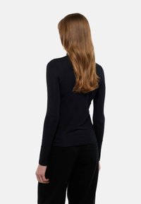 Top noir à manches longues avec une coupe ajustée et une texture douce, présentant un style minimaliste sans motifs ni détails matériels visibles.