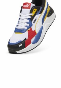 Puma sneakers in white, blue, red, and yellow. Features mesh upper, rubber sole, lace closure, and black accents on the toe and heel.