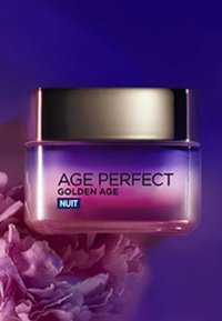 Un pot en verre avec un dégradé allant du violet au rose, doté d'un couvercle doré. L'étiquette indique "AGE PERFECT GOLDEN AGE NUIT." Il est installé sur un fond floral.