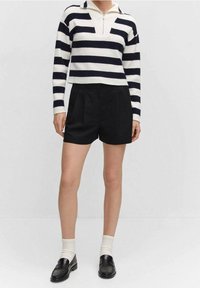 Sweter dzianinowy w paski w kremowym i granatowym kolorze z suwakiem sięgającym ćwierć długości, zestawiony z czarnymi dopasowanymi szortami. Czarne mokasyny i białe skarpetki dopełniają stylizację.