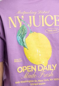 Purple cotton t-shirt featuring a large yellow lemon graphic, green leaf, and yellow text that reads "NY JUICE" and "OPEN DAILY."