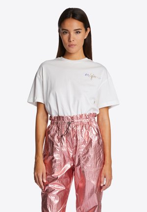 White cotton t-shirt with "california" embroidered in colorful thread, paired with metallic pink, shiny cargo pants featuring an elastic waistband.