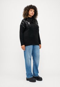 Juodas megztinis su blizgučiais viršutinėje dalyje, laisvas siluetas. Sujungtas su šviesiai mėlynomis džinsais ir juodais masyviais kulnais.