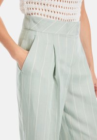 Hellgrüne gestreifte Hose mit strukturiertem Stoff, weitem Bein, hoher Taille, Falten und seitlichen Taschen für funktionale Nutzung.