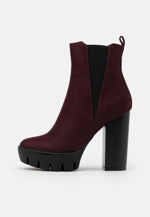 Bordeaux ruskindsankelstøvle med elastiske sidepaneler, en chunky høj hæl og en tyk, rillede sort platformsål.