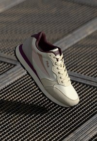 Light beige athletic shoe with a textured finish, maroon accents, and a rubber sole. Features classic lacing and a padded collar.