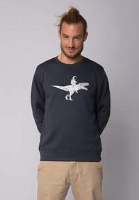 Sweatshirt marine à manches longues avec un graphique blanc représentant un dinosaure et un astronaute. Matière en mélange de coton avec un design à col rond.