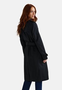 Manteau noir en trench avec une taille ceinturée, col boutonné et manches longues. Texture lisse et design jusqu'aux genoux.