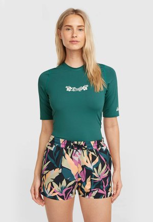 T-shirt anti-éruption vert foncé à manches courtes avec un logo floral, associé à un short coloré arborant un motif de feuilles tropicales et une taille à cordon de serrage.