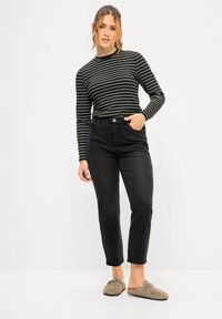 Jeans neri a vita alta con gamba dritta, abbinati a una maglietta a righe in bianco e nero a maniche lunghe. Scarpe slip-on in camoscio casual.
