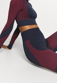 Navy- und burgunderfarbenes Activewear-Set mit einem langärmligen Croptop und hochgeschnittenen Leggings mit strukturierten Mustern und kontrastierenden Einsätzen.