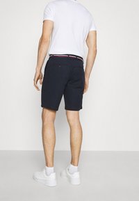 Marina shorts i bomull med en slät textur, försedda med ett bälte med röd och vit rand. Baksidan visar två fickor och en knappdetalj.