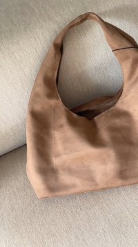 Brun tygkasse med mjuk textur, med ett runt handtag och öppen topp. Minimalistisk design, inga synliga detaljer eller mönster.