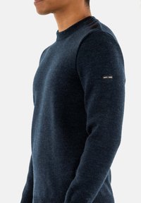 Maglione lavorato a maglia blu navy con collo rotondo, finitura testurizzata e bottoni decorativi sulla spalla. Etichetta del marchio sulla manica.