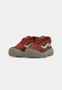 Røde og beige sneakers med gummisåle, teksturert overdel og kontrasterende hvit bølgedesign. Har snørebånd og logo på tungen.