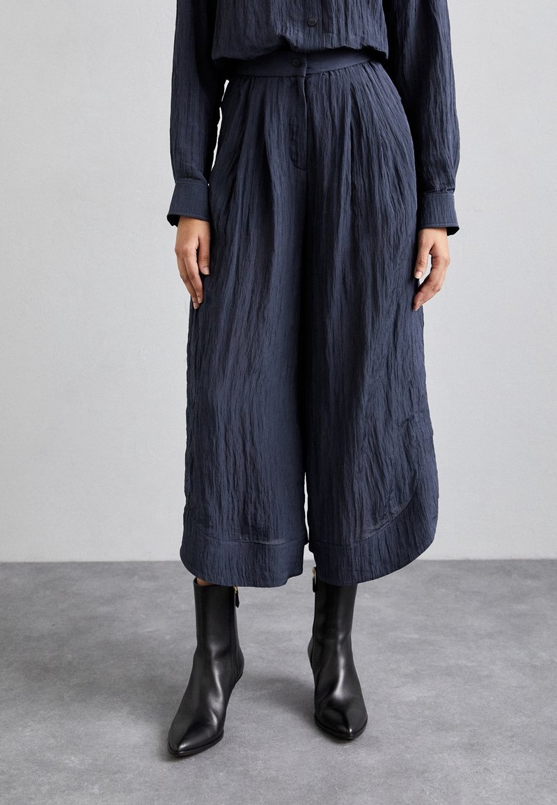 Navy crepe culottes s uvolněným střihem, širokým nohavicemi, záhyby a hladkou texturou, doplněné o černé špičaté kotníkové boty.