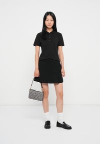 Sort polo t-shirt med korte ærmer, parret med en sort nederdel og sorte loafers. Hvide sokker og en mønstret taske fuldender looket.