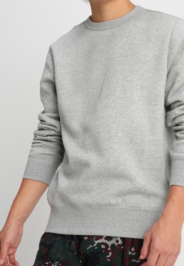 Personne portant un sweat-shirt gris uni à manches longues avec des poignets et un ourlet côtelés, associé à un pantalon camouflage vert foncé et noir.